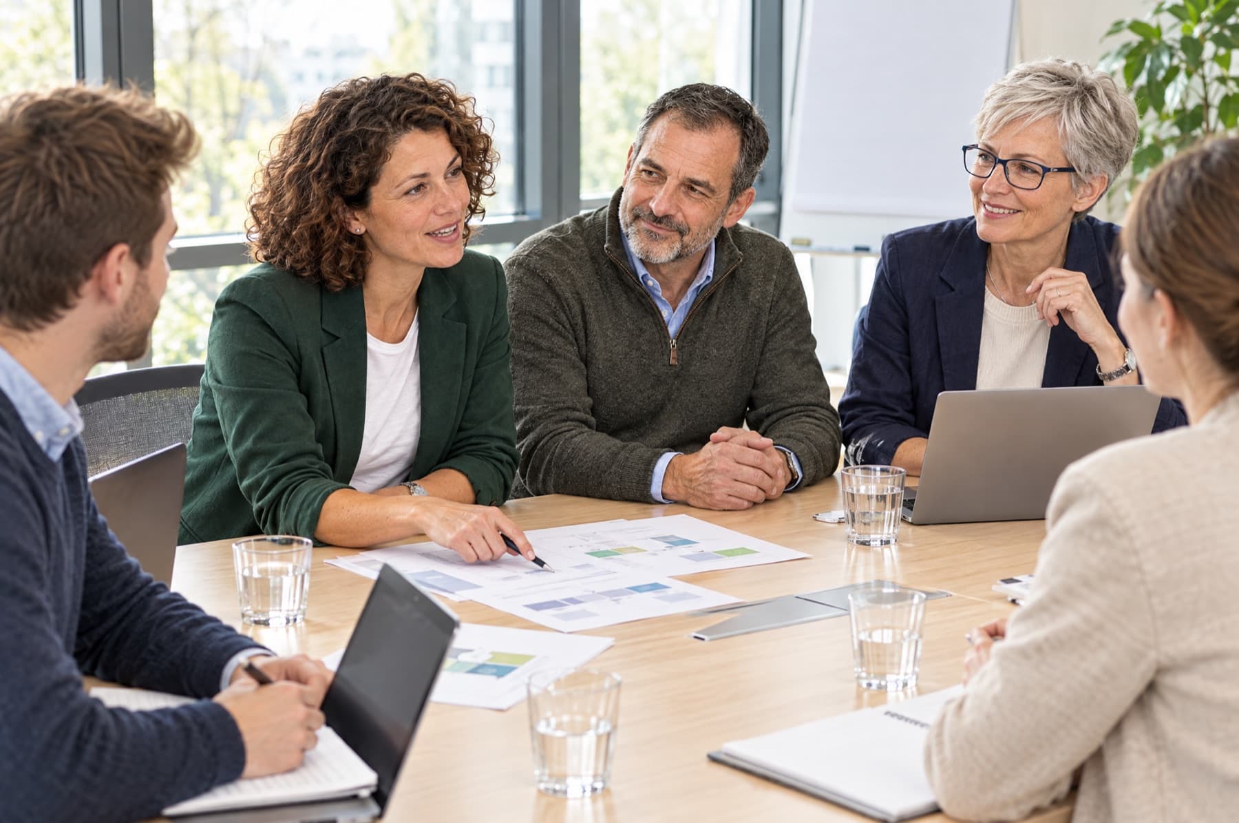 Fünf Case Managerinnen und Case Manager unterschiedlichen Alters besprechen an einem Tisch mit Laptops und Fallplänen einen Fall.